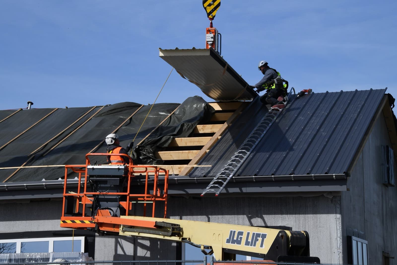 Crane lifting roof panels while workers fit them