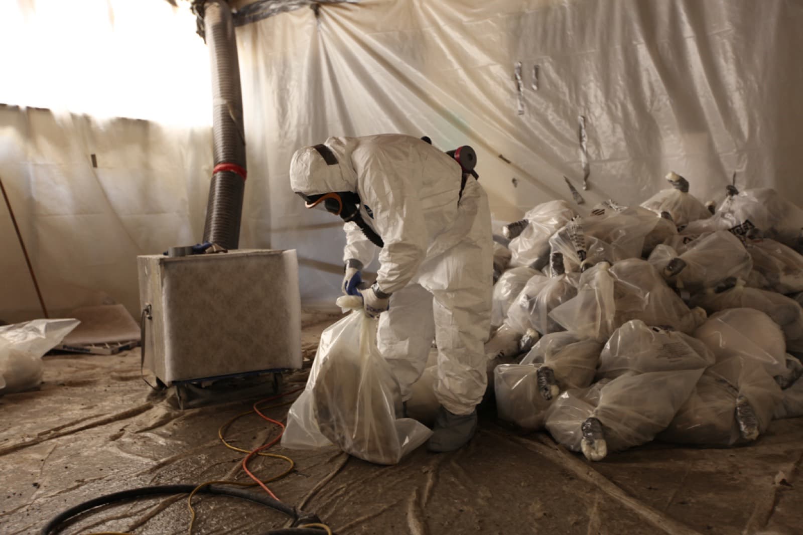 Worker in full PPE bagging asbestos waste in a sealed area