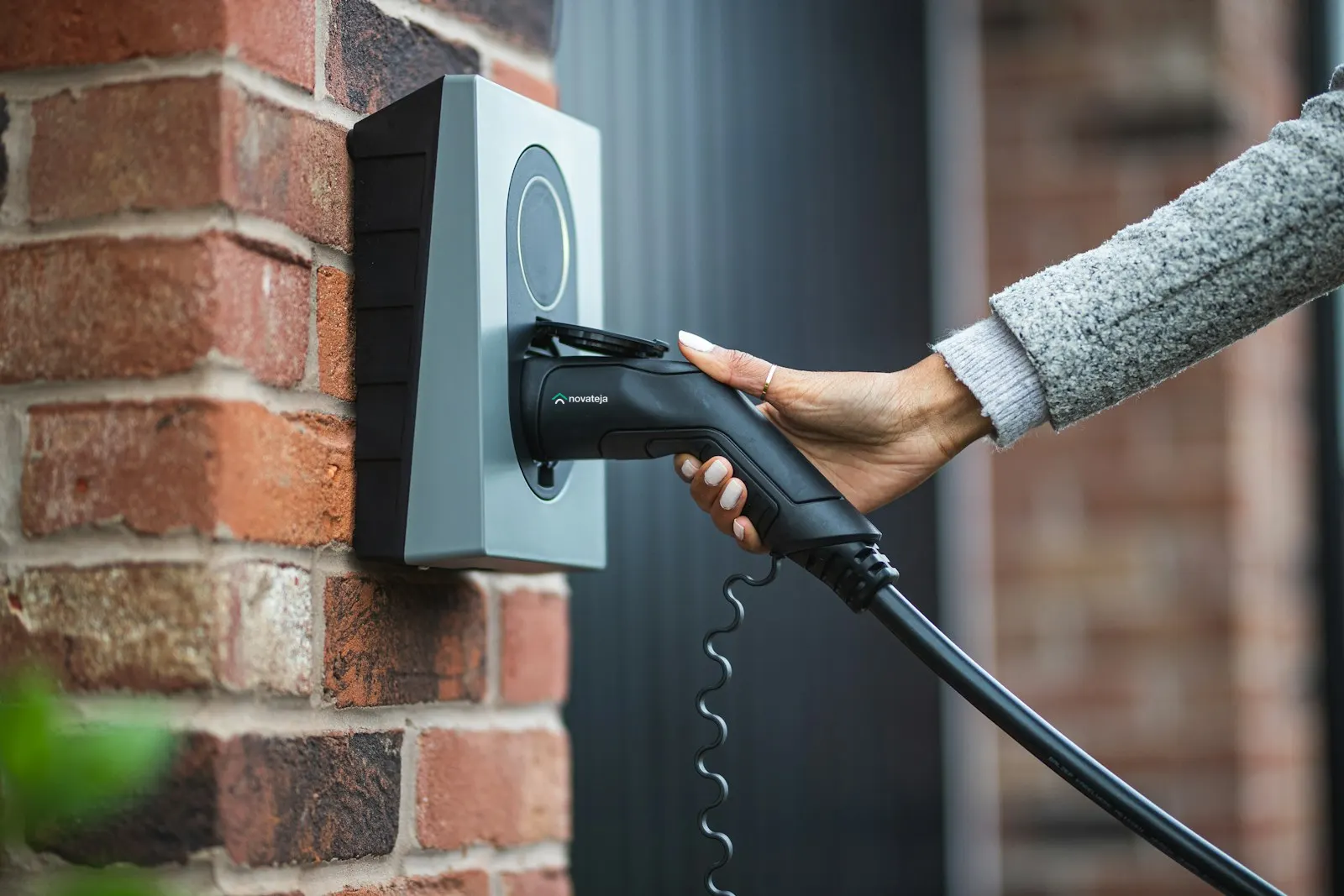 Hand plugging in a wall-mounted EV charger cable